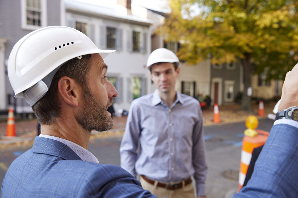 2 people with hard hats stand and point outside