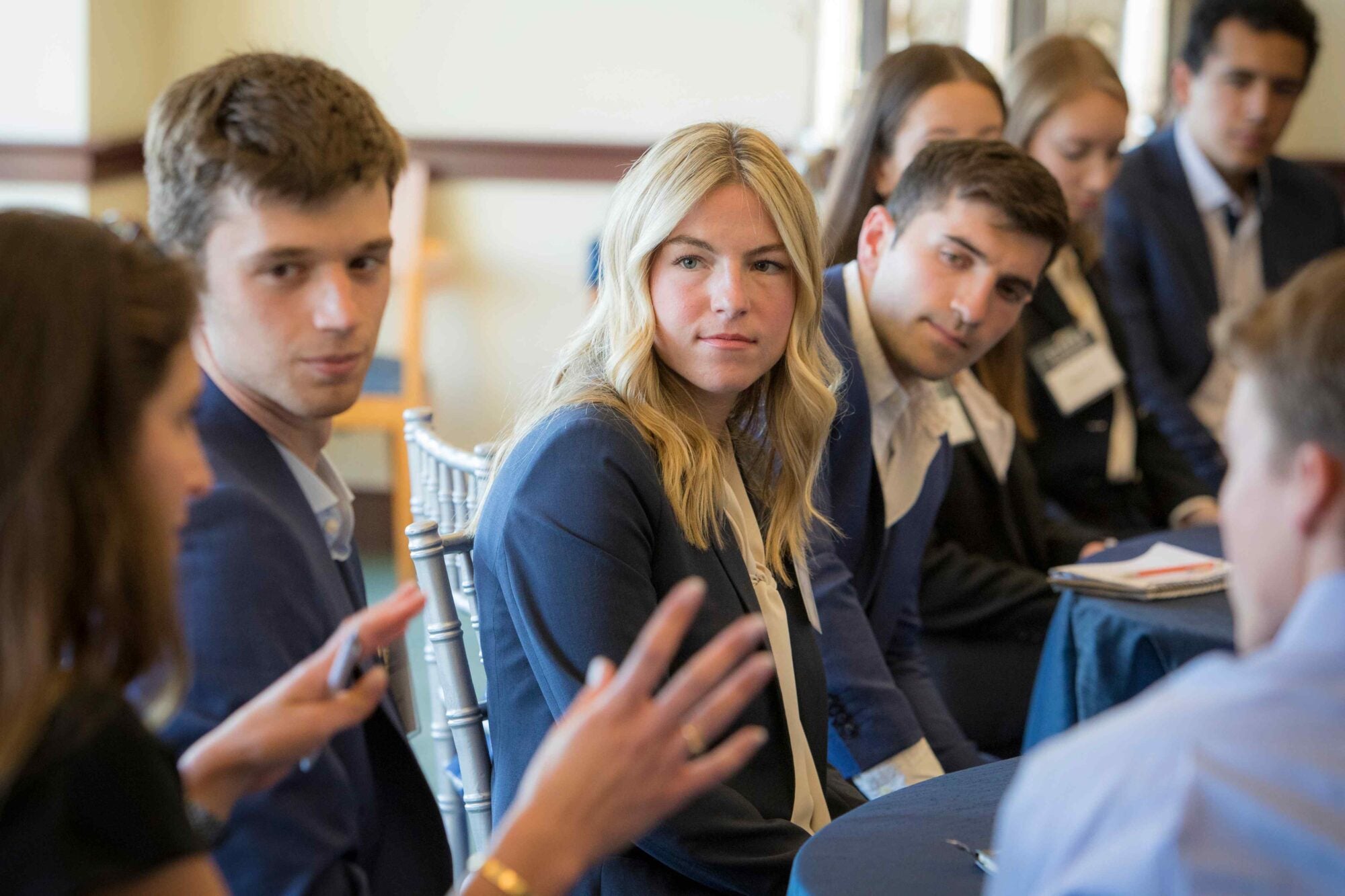 A Steers center student speaks to her peers around a table during a speaker event small group chat in a McDonough School of Business conference room. Well lit space with natural lighting coming from behind the group.